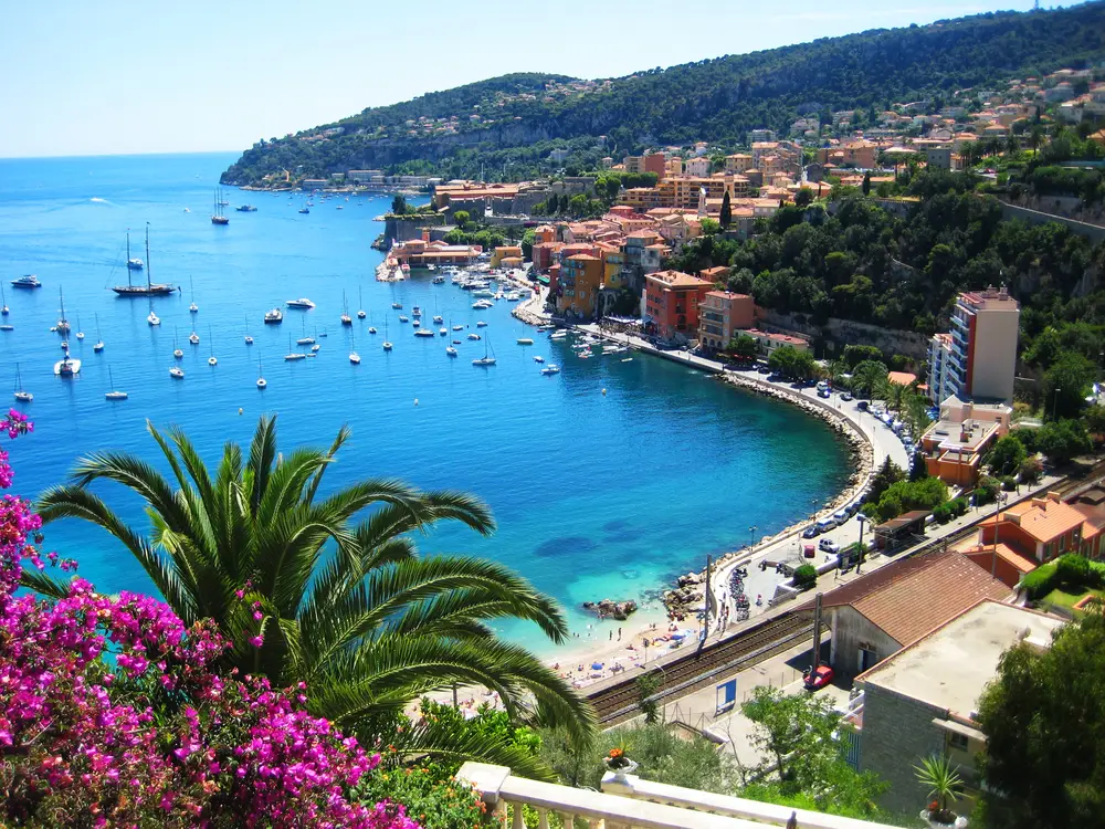 Baia della Costa Azzurra con barche ormeggiate e bouganville in fiore