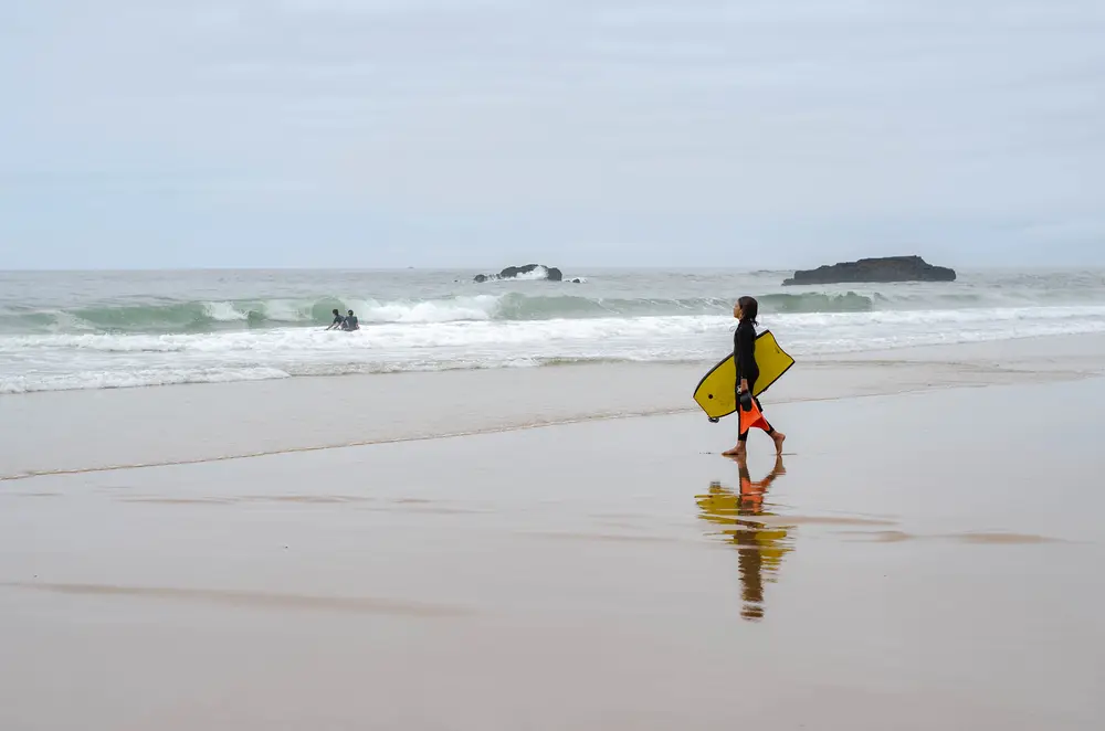 Surfista che cammina sulla spiaggia con la tavola, in Portogallo