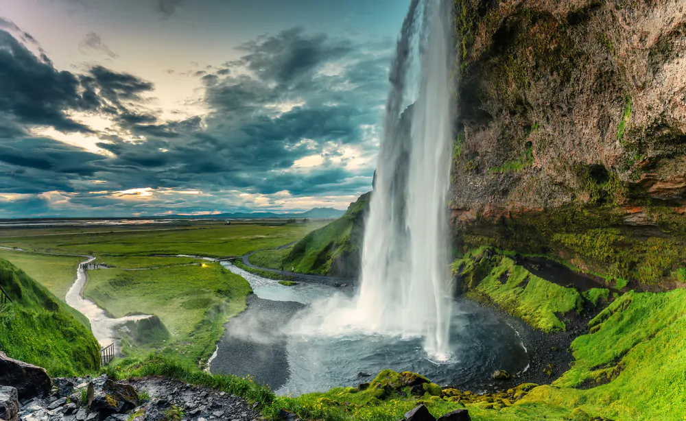 Panoramic landscape of beautiful Seljalandsfoss waterfall flowing and lush field on gloomy day in summer at Iceland